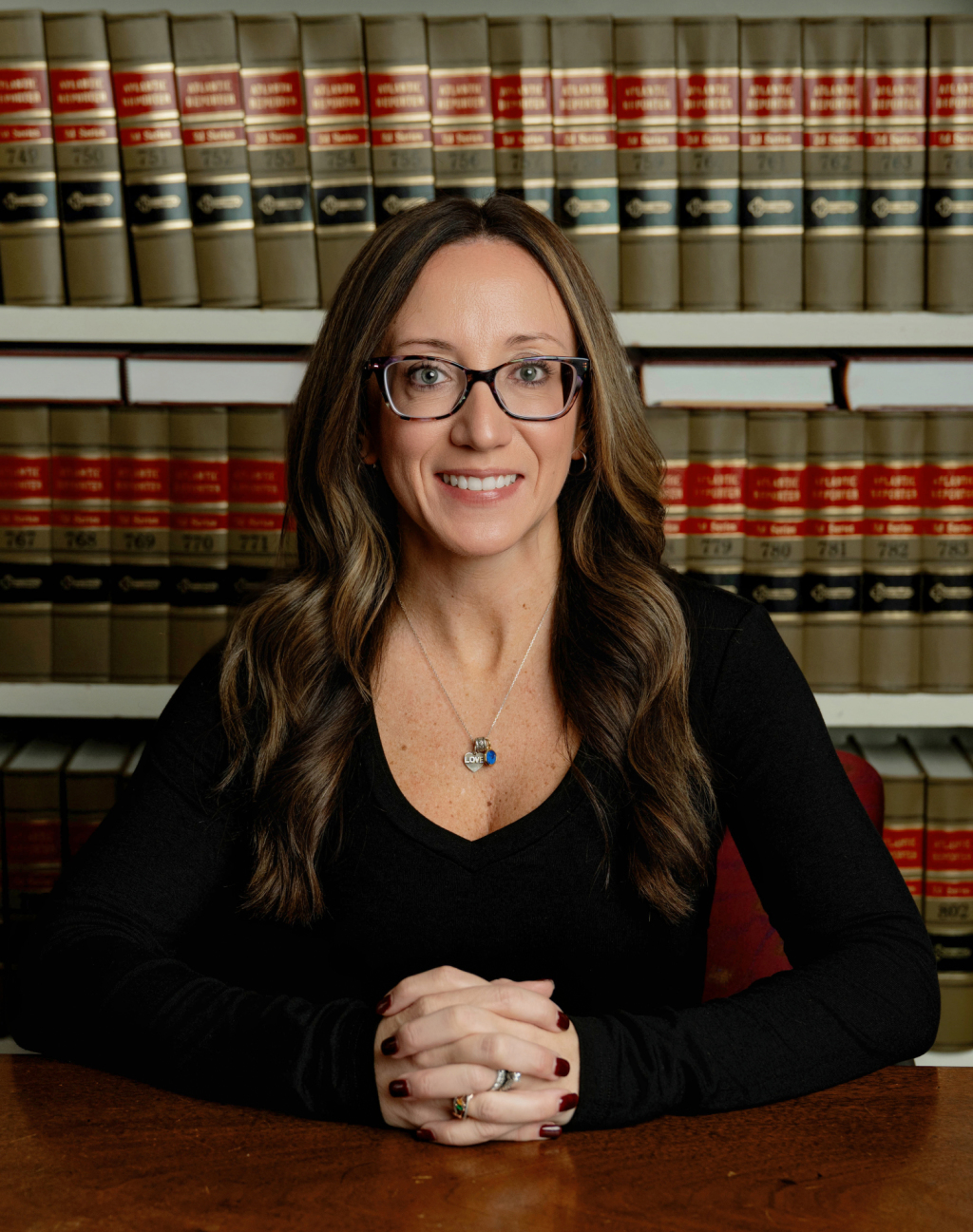 Portrait of Personal Injury Law Office Manager and Paralegal Ashley Inverso smiling in front of a case of legal books.