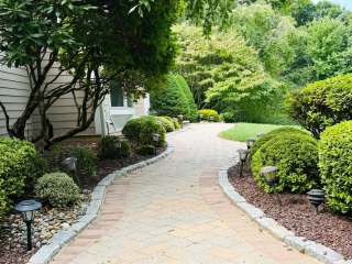 Curved paver walkway with warm-toned borders, stone edging and mature shrubs.