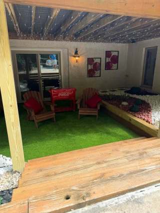Covered seating area beneath a deck with red chairs and green ground covering.