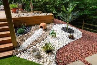 Curved white and red stone beds with a tipped decorative pot beside wooden deck steps.