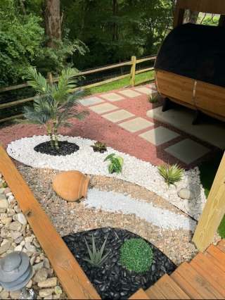 Curved white and red stone beds with a tipped decorative pot beside wooden deck steps.