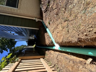 Solid drainage pipe connected to a gutter downspout in an open trench beside a Wilmington DE house