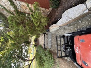 Tracked loader beside an unfinished walkway with natural stone steps and matching boulders in place