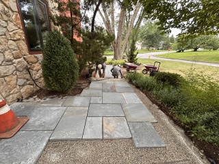 Crew laying rectangular bluestone pieces along a walkway beside established garden beds