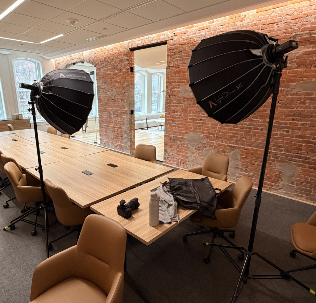 Behind-the-scenes view of a simple two-light headshot setup inside a conference room with exposed brick walls