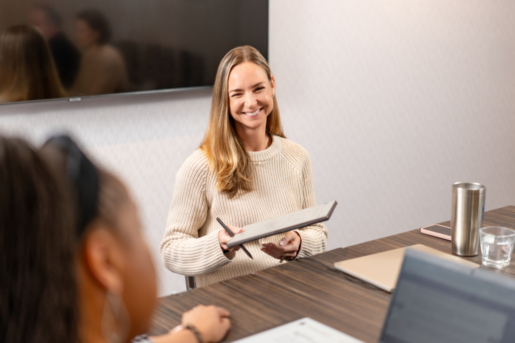 Woman smiling and handing an electronic tablet to a client.
