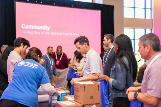 Participants assembling blue bags during a United Way community project, with the project’s presentation screen behind them.