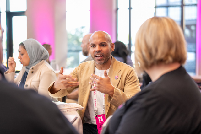 Attendee in a tan jacket gesturing during a small-group conversation at the Leadership Institute.
