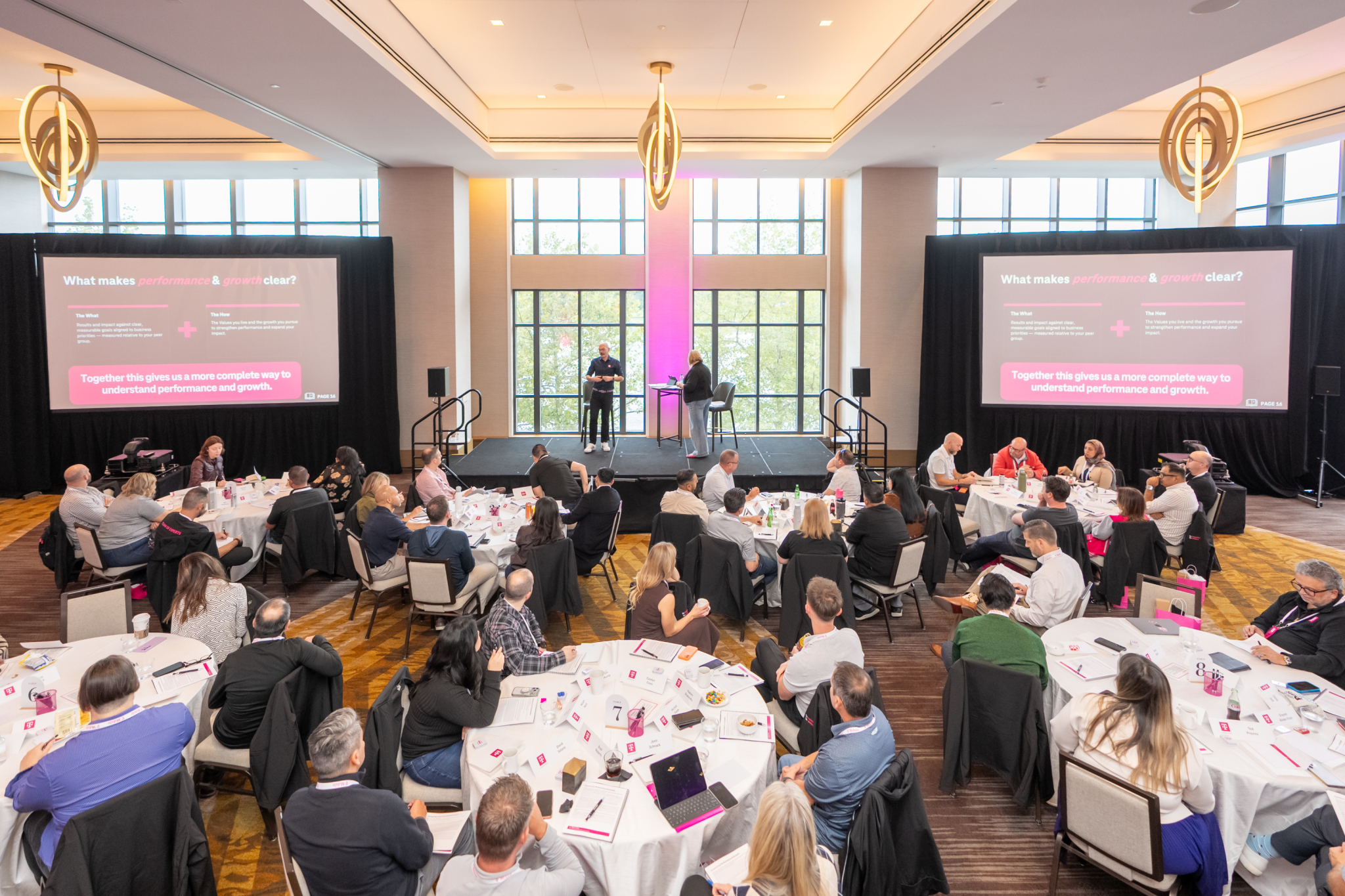 Elevated view of the Leadership Institute ballroom, with attendees at round tables facing the stage and two presentation screens.
