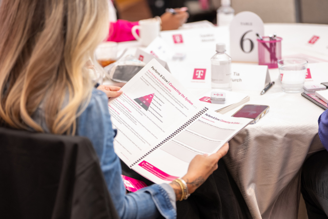 Attendee reading the event’s leadership workbook at a table with T-Mobile-branded materials.