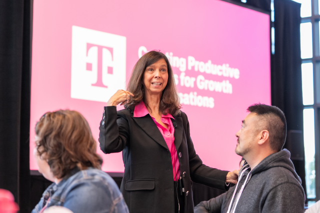 Facilitator speaking among seated participants beside a T-Mobile presentation screen.